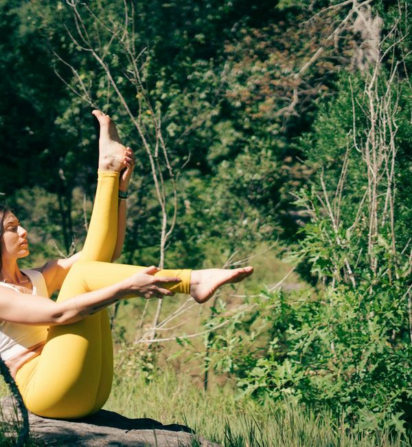 Woman performing a gentle yoga stretch outdoors, surrounded by nature and sunlight.